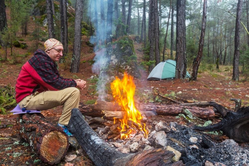 Man at winter camp in front of fire